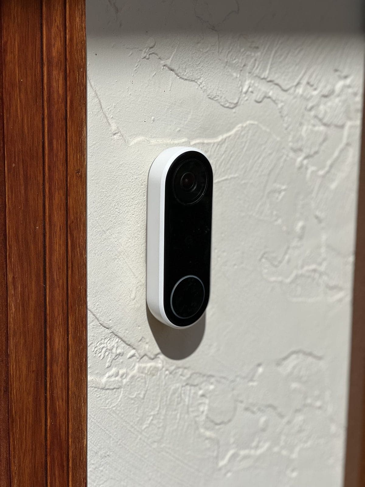 Google Nest doorbell on stucco by wood door frame